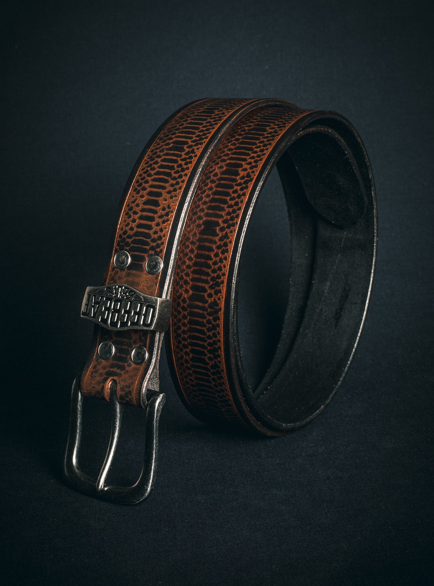Brown embossed leather belt with silver buckle on a dark background